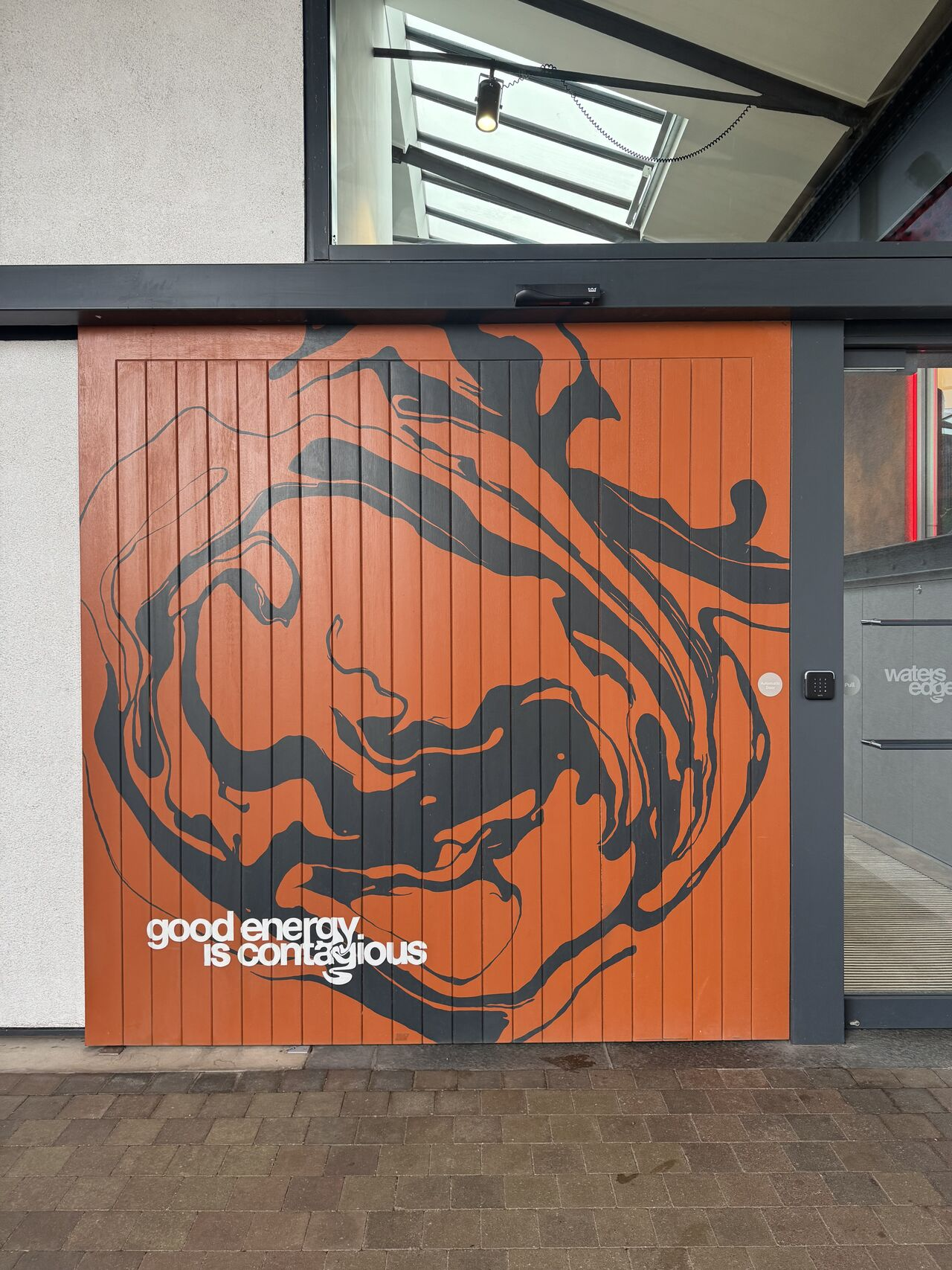 Water's Edge building exterior in Dundee featuring an orange mural with flowing abstract shapes and the phrase 'good energy is contagious'